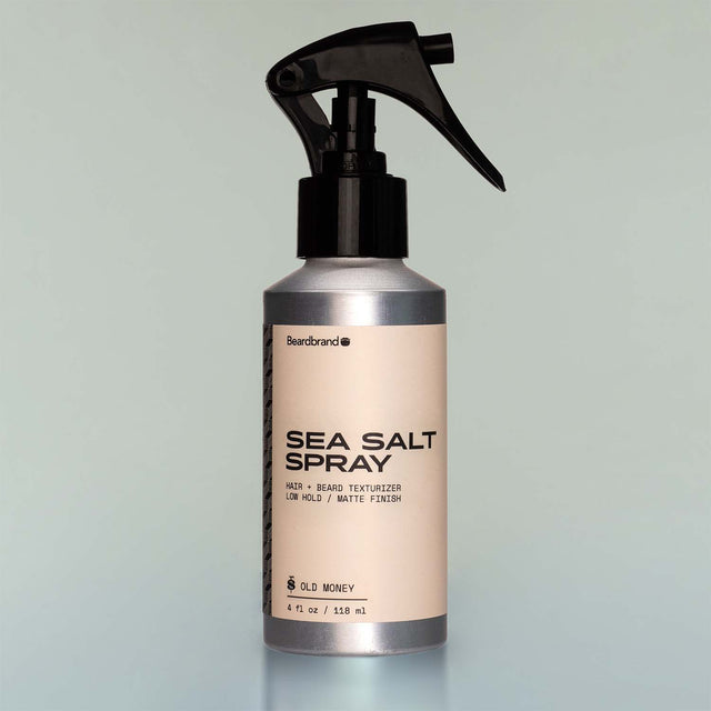 A bottle of Old Money Sea Salt Spray with a sprayer dispenser against a grey background.